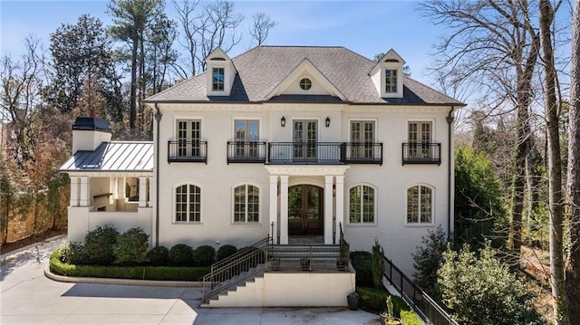 view of front facade featuring french doors, brick siding, a standing seam roof, metal roof, and a balcony