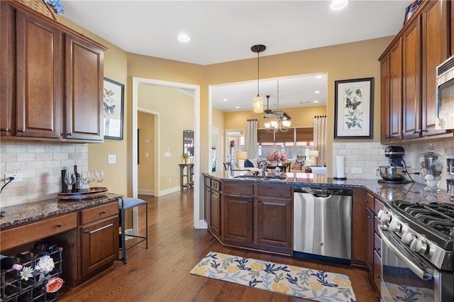 kitchen featuring a sink, dark stone countertops, dark wood finished floors, backsplash, and appliances with stainless steel finishes