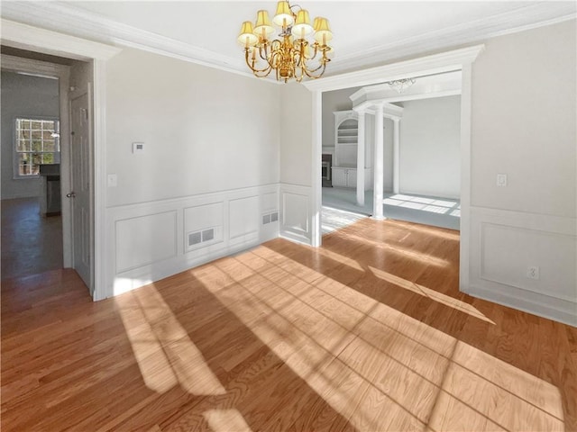 empty room with ornate columns, crown molding, hardwood / wood-style floors, and a chandelier