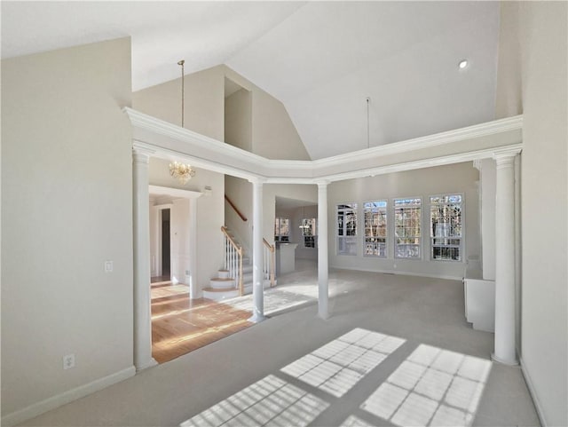 carpeted spare room featuring ornate columns, high vaulted ceiling, and a chandelier