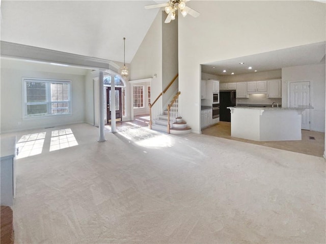 unfurnished living room with ceiling fan, light colored carpet, and high vaulted ceiling