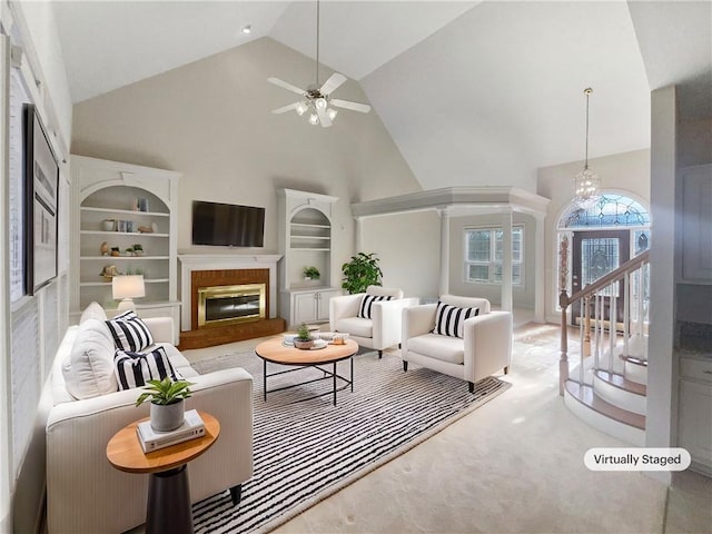 carpeted living room with ceiling fan with notable chandelier, built in features, and high vaulted ceiling