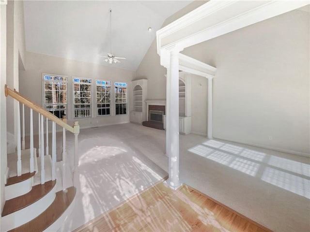 unfurnished living room with ceiling fan, carpet floors, high vaulted ceiling, and ornate columns