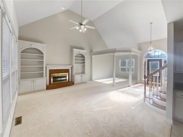 unfurnished living room featuring ceiling fan with notable chandelier, high vaulted ceiling, a brick fireplace, light carpet, and built in shelves