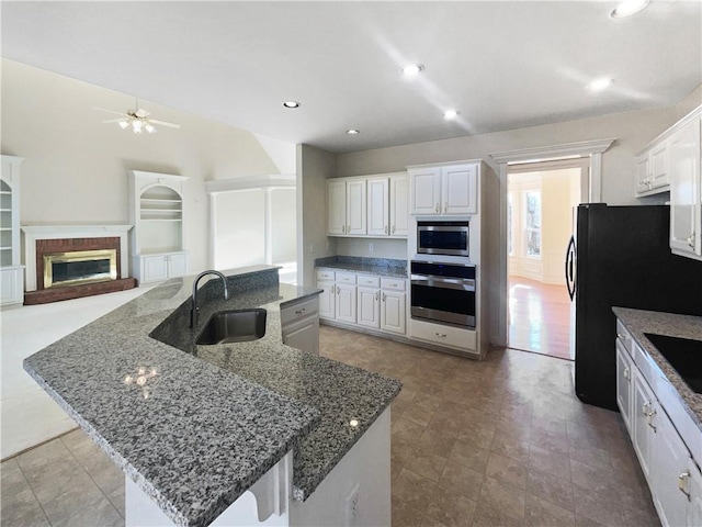 3905 Colonial Trl SW, Lilburn, GA 30047 - kitchen with black appliances, a sink, a ceiling fan, a center island with sink, and dark stone countertops