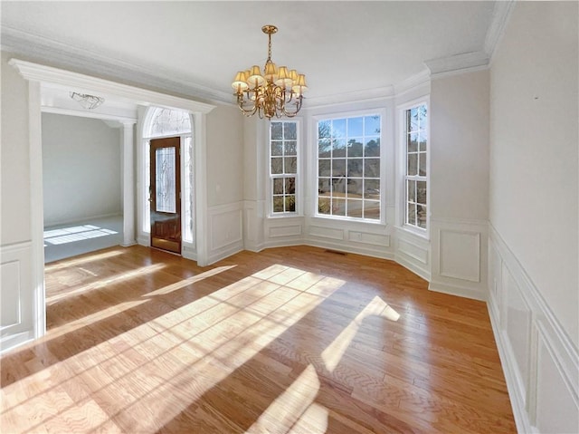 unfurnished dining area with a notable chandelier, light hardwood / wood-style flooring, ornamental molding, and decorative columns