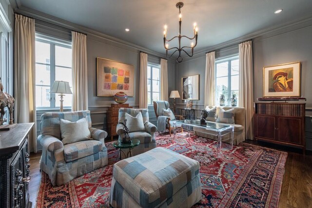 living area featuring wainscoting, a decorative wall, crown molding, dark wood-type flooring, and a notable chandelier