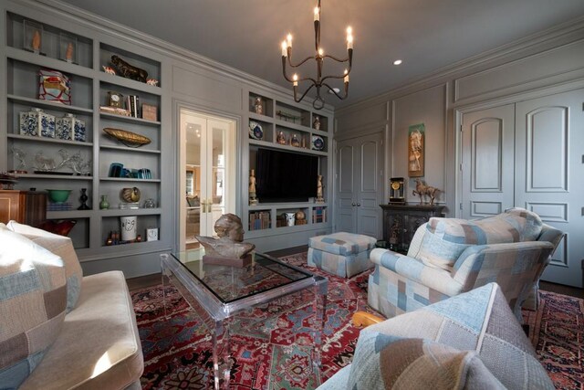 living room featuring an inviting chandelier, ornamental molding, a decorative wall, and built in features