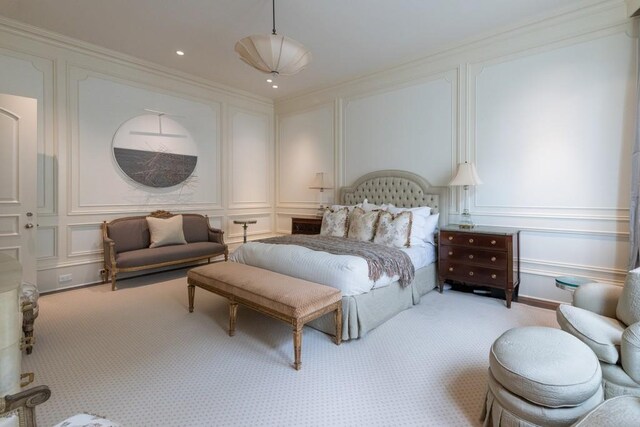 bedroom with a decorative wall, ornamental molding, and light carpet