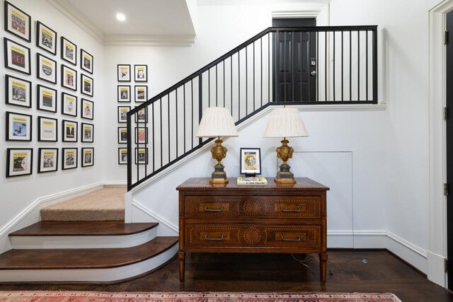 staircase with wood finished floors and ornamental molding