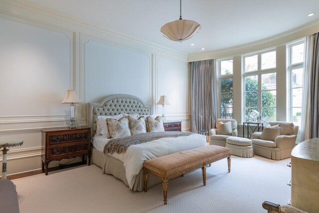 bedroom with crown molding, a decorative wall, and light colored carpet