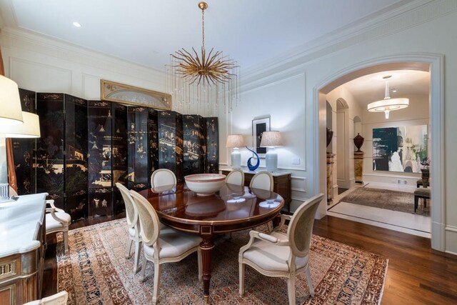 dining area featuring a decorative wall, arched walkways, wood finished floors, and ornamental molding