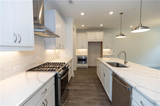 kitchen with sink, white cabinetry, light stone counters, appliances with stainless steel finishes, and wall chimney range hood