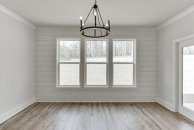 unfurnished dining area with a chandelier, light wood-style floors, crown molding, and baseboards