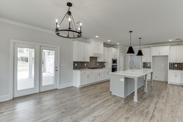 kitchen with backsplash, a chandelier, white cabinetry, light countertops, and light wood-style flooring