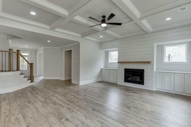 unfurnished living room with a ceiling fan, light wood-style flooring, a large fireplace, beamed ceiling, and stairway