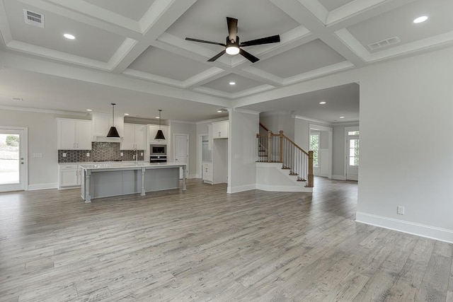 unfurnished living room featuring light wood-style flooring, stairway, ceiling fan, baseboards, and beamed ceiling