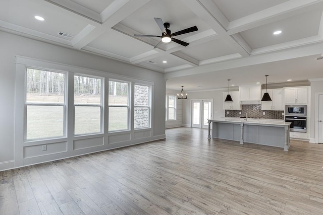 living area featuring light wood-style flooring, ceiling fan, coffered ceiling, beam ceiling, and a chandelier