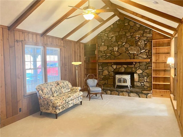 sitting room featuring carpet, ceiling fan, lofted ceiling with beams, a wood stove, and wood walls