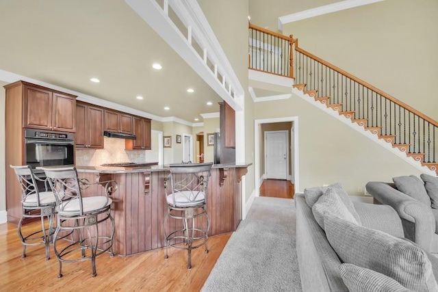 2740 Heritage Bend Ct SW, Grayson, GA 30017 - kitchen with oven, ornamental molding, open floor plan, light wood-type flooring, and under cabinet range hood