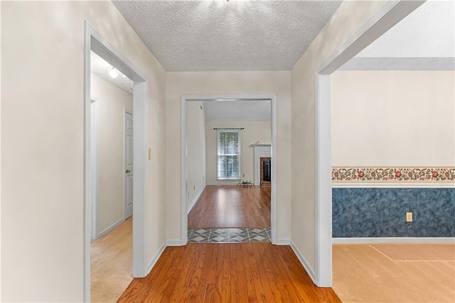 hall with a textured ceiling, light wood finished floors, and baseboards