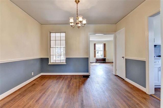 unfurnished dining area with wood finished floors, baseboards, and a chandelier