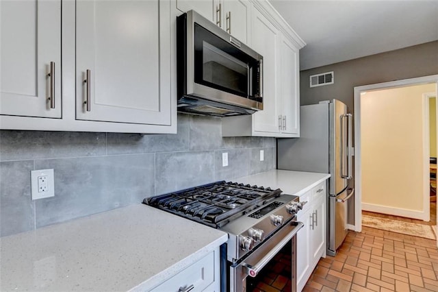 kitchen featuring visible vents, light stone counters, decorative backsplash, stainless steel appliances, and white cabinetry