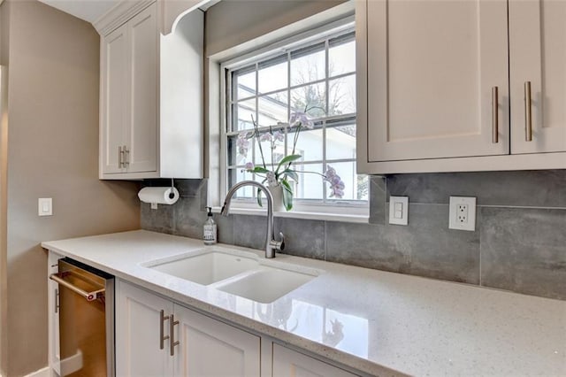 kitchen with light stone counters, white cabinetry, a sink, dishwasher, and tasteful backsplash