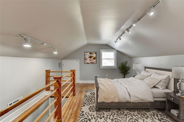 bedroom featuring visible vents, wood finished floors, track lighting, and vaulted ceiling