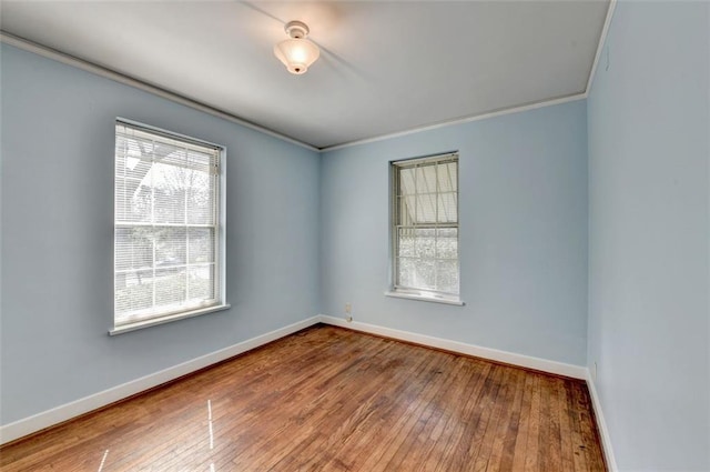 empty room featuring hardwood / wood-style floors, crown molding, and baseboards