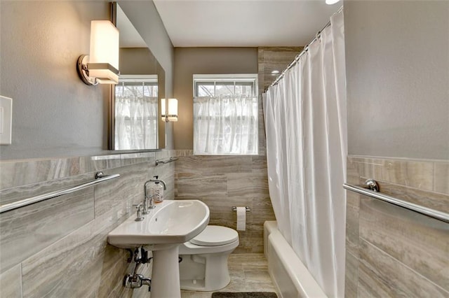 bathroom with shower / bathtub combination with curtain, a wainscoted wall, a sink, tile walls, and toilet