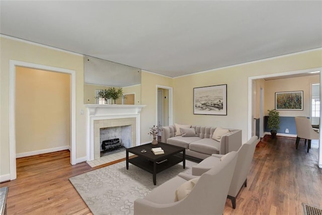 living area featuring wood finished floors, visible vents, baseboards, a fireplace, and crown molding