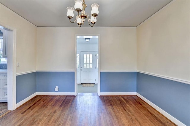 unfurnished dining area featuring a notable chandelier, baseboards, and wood finished floors