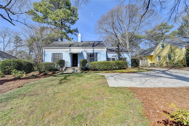 view of front facade featuring driveway, a chimney, and a front yard