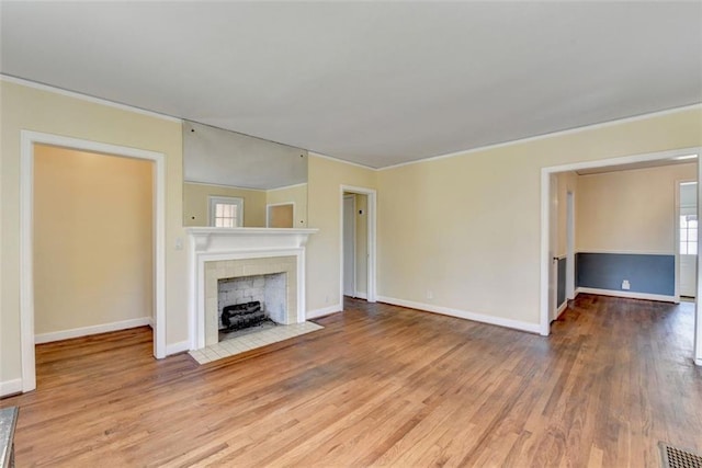 unfurnished living room with visible vents, baseboards, wood finished floors, and a tiled fireplace