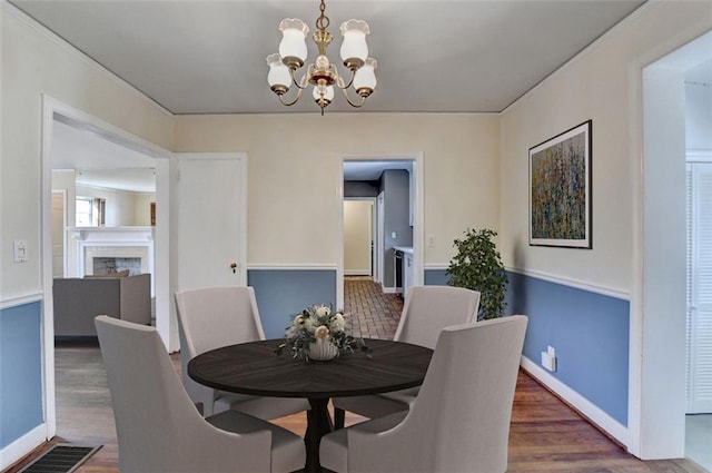 dining space featuring a chandelier, visible vents, a fireplace, and wood finished floors