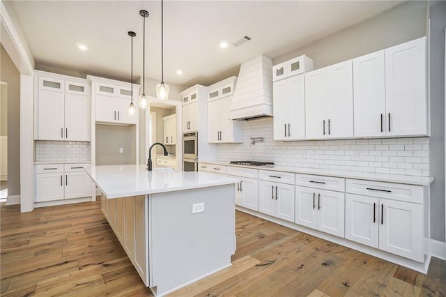 kitchen with custom range hood, appliances with stainless steel finishes, decorative backsplash, light wood-style floors, and light countertops