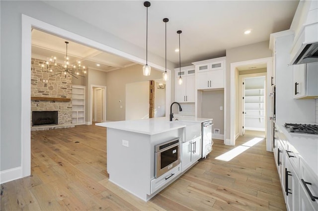 kitchen with stainless steel gas cooktop, light wood finished floors, open floor plan, a chandelier, and glass insert cabinets
