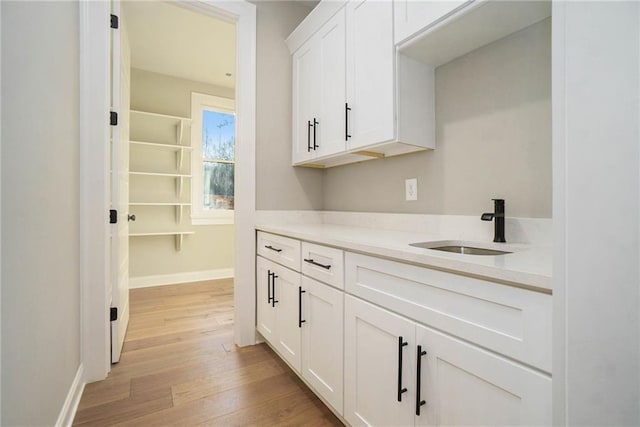 kitchen featuring a sink, light wood-type flooring, white cabinets, light countertops, and baseboards