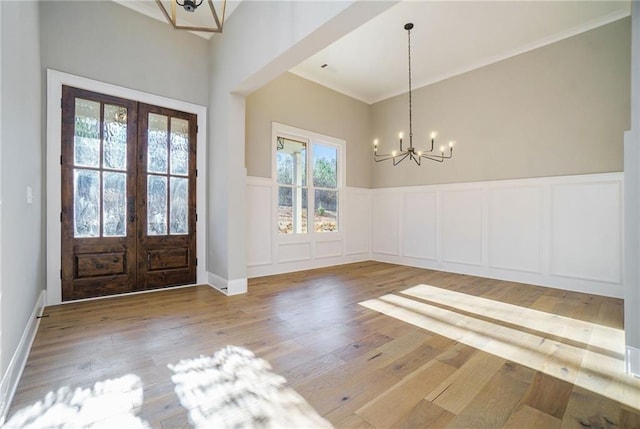 foyer entrance with a chandelier, french doors, ornamental molding, a decorative wall, and a wainscoted wall