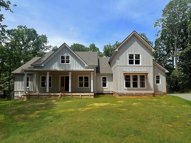 rear view of house featuring roof with shingles, board and batten siding, a lawn, and covered porch
