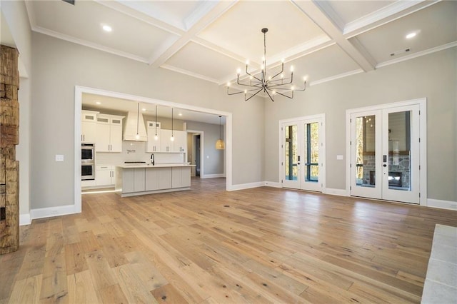 unfurnished living room featuring french doors, coffered ceiling, light wood-style floors, a chandelier, and beamed ceiling