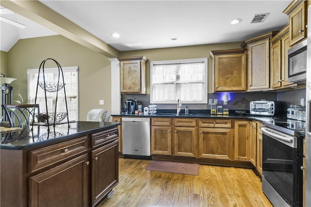 kitchen with dark stone counters, stainless steel appliances, sink, light hardwood / wood-style floors, and lofted ceiling