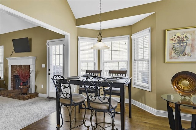 dining room with vaulted ceiling, a fireplace, dark wood-type flooring, and plenty of natural light