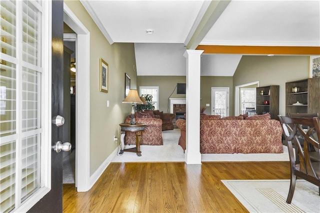 entryway with ornate columns, crown molding, hardwood / wood-style floors, lofted ceiling, and a fireplace