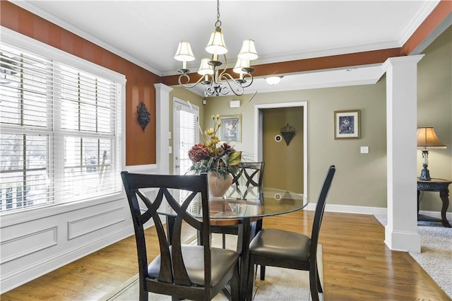 dining area featuring hardwood / wood-style flooring, a notable chandelier, ornate columns, and crown molding