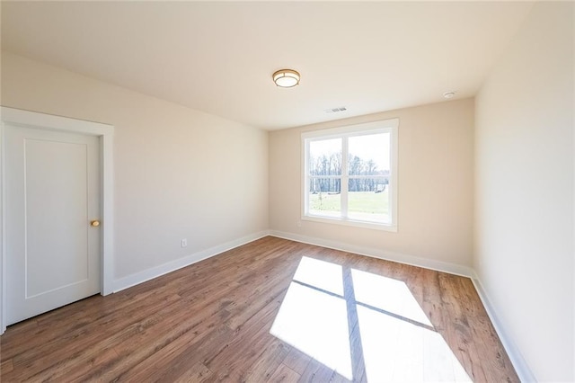 spare room featuring visible vents, baseboards, and wood finished floors