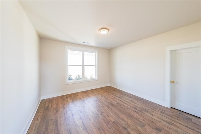 empty room featuring visible vents, baseboards, and wood finished floors