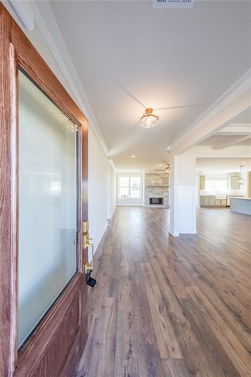 unfurnished living room with a large fireplace, ornamental molding, wood finished floors, and visible vents