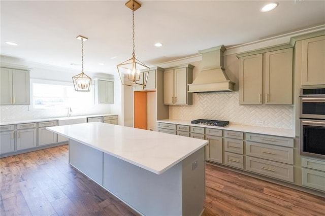 kitchen featuring appliances with stainless steel finishes, a center island, hanging light fixtures, custom exhaust hood, and light countertops